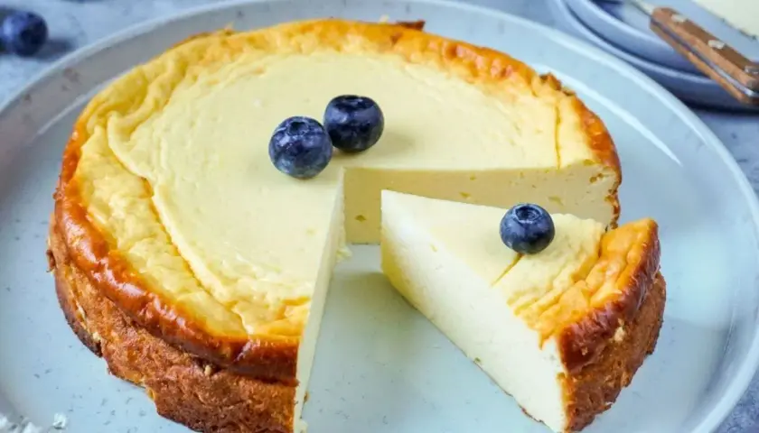 Leckerer protein cheesecake aus magerquark, garniert mit Blaubeeren. Ein Stück ist bereits angeschnitten.