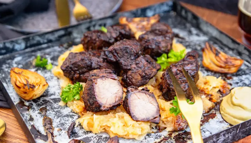 Herzhaftes Mutzbraten Rezept Original: Dunkles, saftiges Fleisch auf Sauerkraut, garniert mit Petersilie und gerösteten Zwiebeln. Ein Festmahl!