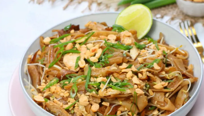 Schüssel mit Pad Thai Gai, garniert mit Erdnüssen und Frühlingszwiebeln, dazu eine Limettenspalte.
