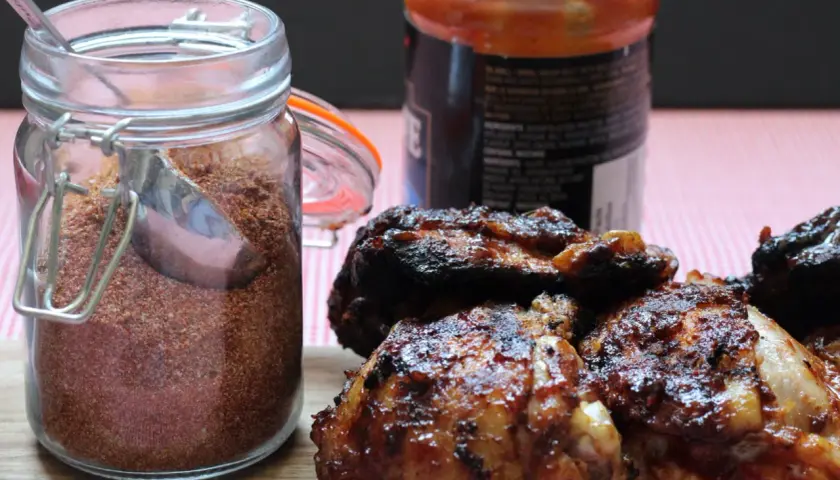 Glas mit Gewürzmischung, perfekt für ein magic dust rezept. Daneben saftige, gegrillte Hähnchenteile und eine Flasche BBQ-Sauce.
