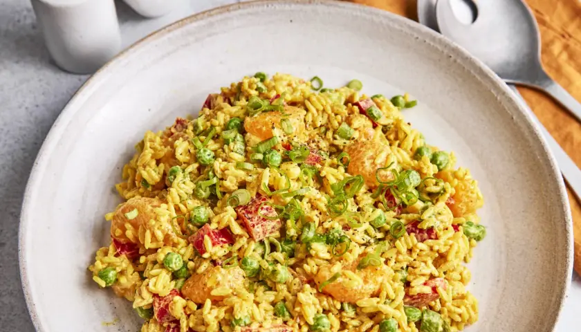 Ein Teller mit weltbestem Reissalat mit Curry, garniert mit Erbsen, Paprika und Frühlingszwiebeln.