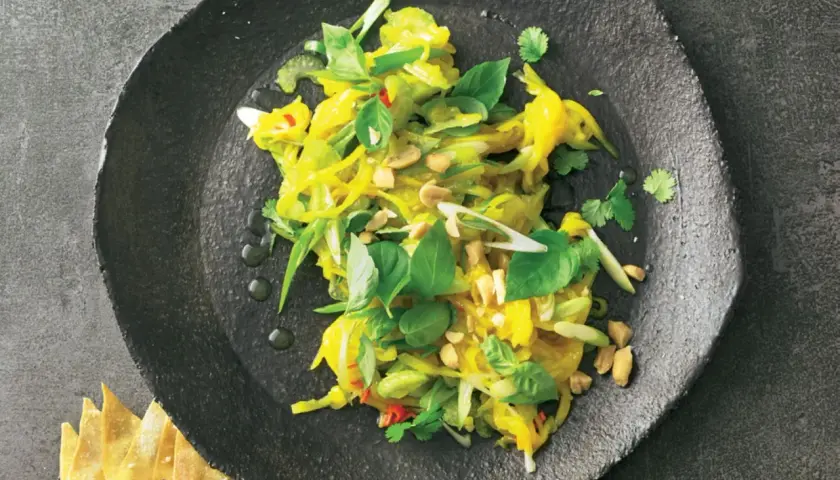 Ein bunter, frischer Mango Salat Thai mit Erdnüssen und Kräutern auf einem dunklen Teller.