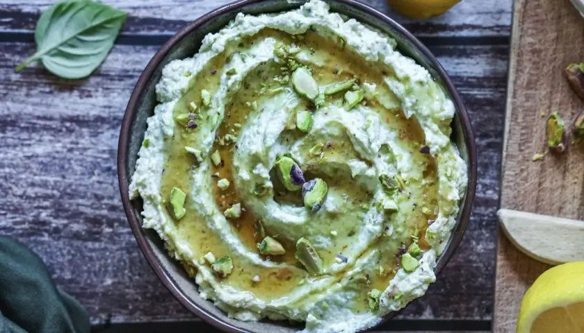 Cremiges Avocado Basilikum Pesto mit Pistazien und Honig beträufelt, garniert mit frischen Basilikumblättern und Zitronenspalten.
