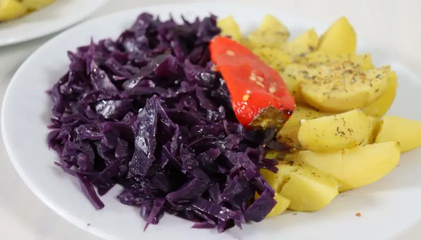 Rotkohl-Rezepte mal anders: Ein Teller mit deftigem Rotkohl, Kartoffelspalten und einer roten Paprika.