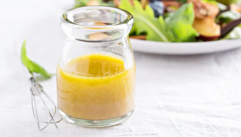 Ein Glas mit gelber Vinaigrette, daneben ein Schneebesen. Ein einfaches vinaigrette rezept für frische Salate.