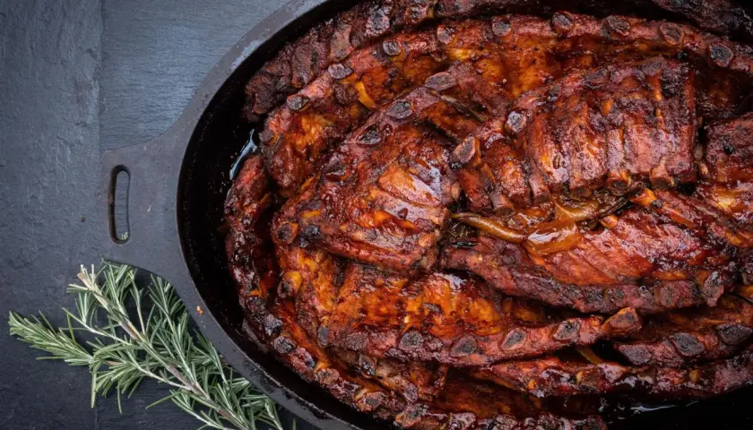 Saftige Spareribs, glasiert und geschmort im Dutch Oven, dane ein Rosmarinzweig.