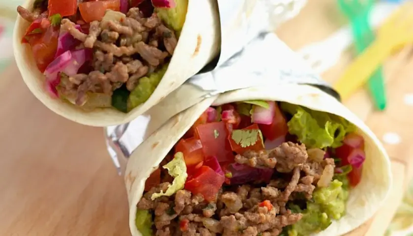 Zwei saftige wraps mit hackfleisch, Guacamole, Tomaten und roten Zwiebeln, eingewickelt in Folie.
