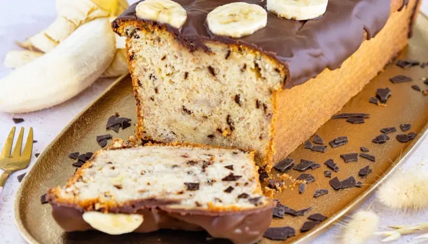 Saftiger Bananen Buttermilch Kuchen mit Schokoladenglasur und Bananenscheiben, garniert mit Schokostückchen.