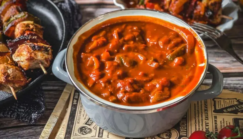 Herzhafte schaschlik sauce wie im imbiss, mit Fleischstücken und Paprika, dane daneben gegrillte Spieße.