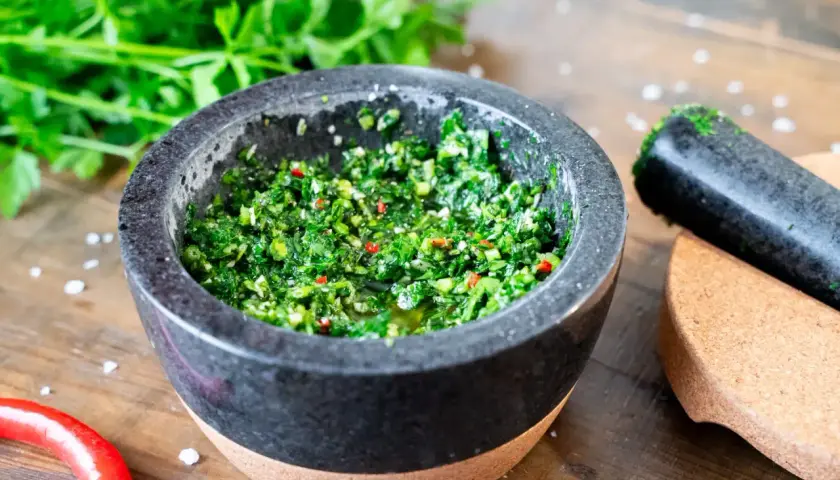 Frisches Chimichurri-Rezept im Mörser, bereit zum Verfeinern von Grillgut. Kräuter, Chili und Öl duften verführerisch.