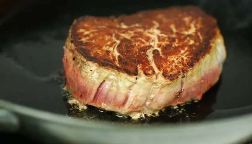 Ein saftiges Steak brät in einer Pfanne. Die Kruste ist goldbraun, das Innere noch rosa. Perfekt, um ein Steak richtig braten zu lernen.