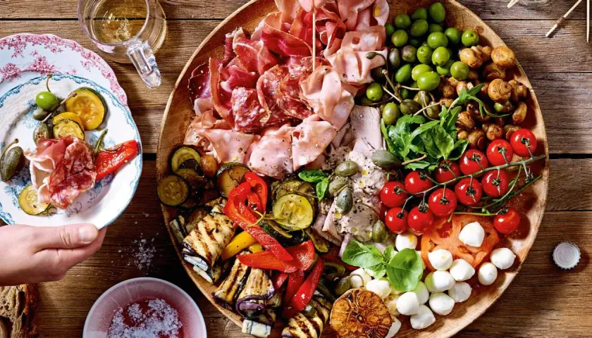 Vielfältige Antipasti Platte Ideen: Wurst, Käse, Oliven, gegrilltes Gemüse und frische Tomaten auf rustikalem Holzbrett.