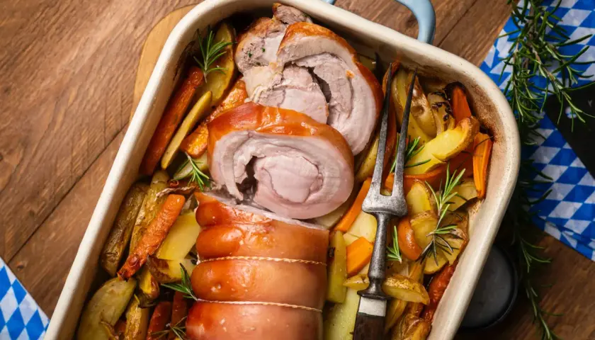 Saftiger **Rollbraten im Backofen** mit Rosmarinkartoffeln und Karotten, bereit zum Servieren.