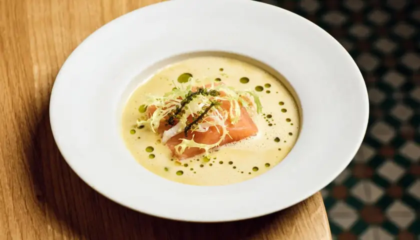 Ein Teller mit Lachs auf cremigem beurre blanc, garniert mit Salat und Kaviar.