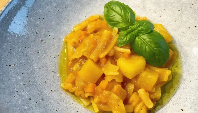 Herzhaftes Pasta e Patate mit Kartoffelstücken, Nudeln und frischem Basilikum in Olivenöl, serviert in einer grauen Schale.