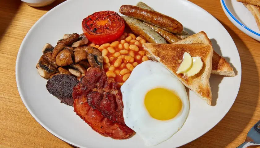 Ein üppiges **full English breakfast** mit Spiegelei, Speck, Würstchen, Bohnen, Pilzen, Tomate, Blutwurst und Toast.