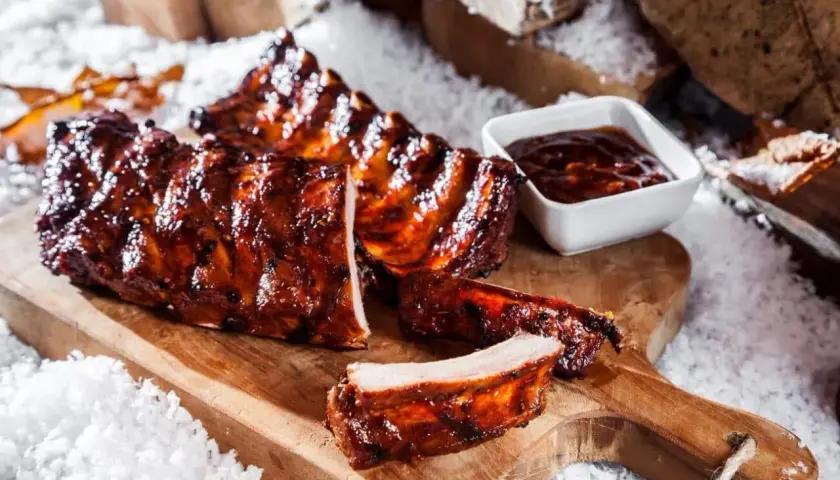 Saftige rippchen im backofen, glasiert und mit BBQ-Sauce, auf einem Holzbrett mit Schnee dekoriert.