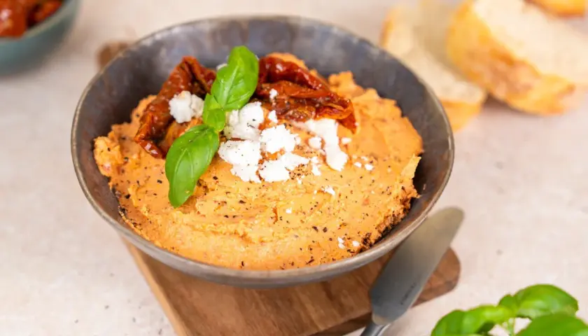 Ein cremiger Tomaten Feta Dip, garniert mit getrockneten Tomaten und Basilikum. Perfekt zum Dippen mit Brot.
