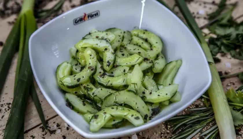 Frischer gurkensalat mit dill, garniert mit Pfeffer und Kräutern, serviert in einer weißen Schüssel.