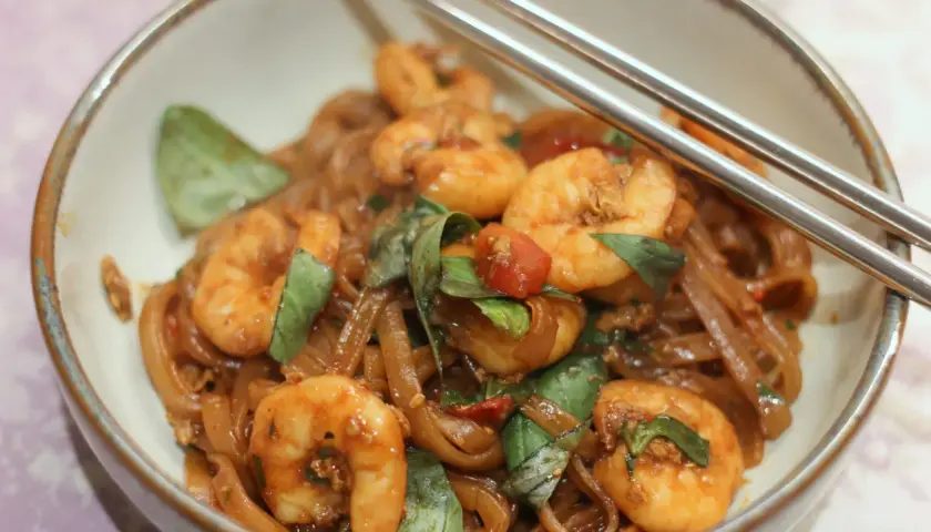 Pad Kee Mao mit Garnelen, Reisnudeln, Basilikum und Tomaten in einer Schüssel, bereit zum Genießen.
