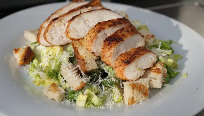 Saftiges Hähnchenbrustfilet auf knackigem Salat mit Croutons und Parmesan – ein klassischer Caesar Salad.