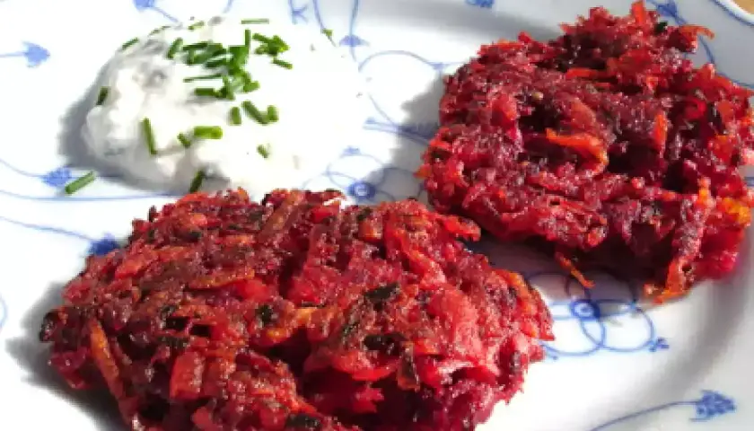 Zwei knusprige rote Bete Puffer paniert, serviert mit einem Klecks Kräuterquark auf einem Teller mit blauem Muster.