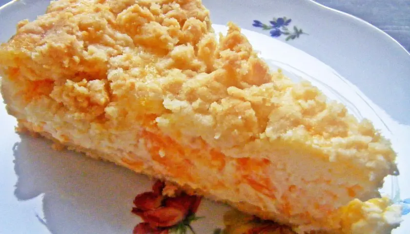 Ein Stück Mandarine Schmand Kuchen mit Streuseln auf einem Teller mit Blumenmuster.