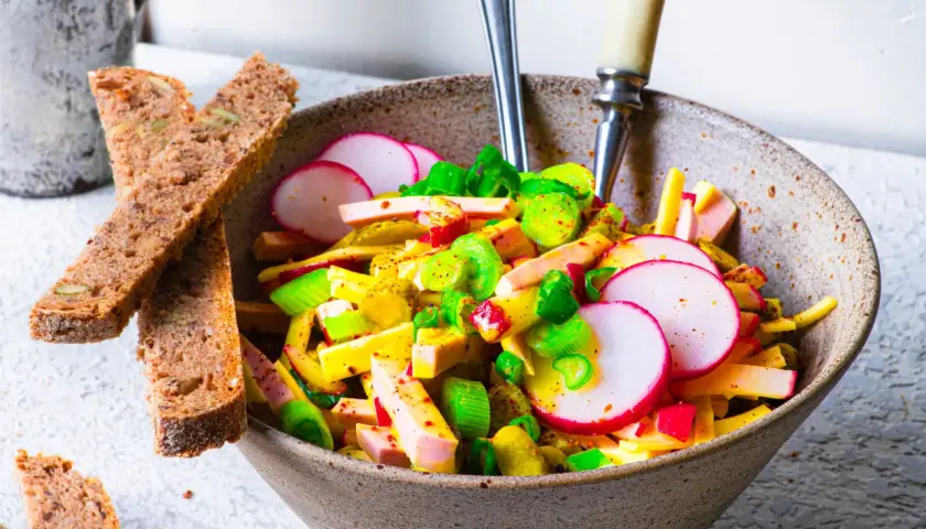 Schmackhafter Schweizer Wurstsalat mit Radieschen und Lauchzwiebeln, serviert mit Vollkornbrot. Ein tolles Rezept für den Sommer!