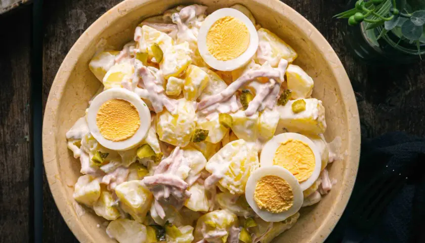 Schüssel mit Kartoffelsalat und Fleischsalat, garniert mit hartgekochten Eiern und Gewürzgurken.