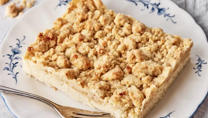 Ein Stück Streuselkuchen, wie von Oma nach DDR-Rezept, mit knusprigen Streuseln auf einem Teller mit blauem Rand.