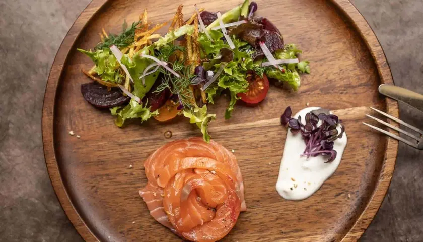 Gebeizter Lachs als Vorspeise, serviert mit einem frischen Salat und cremiger Sauce auf einem Holzbrett.