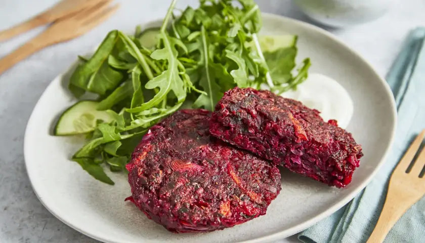 Zwei herzhafte rote Bete Bratlinge auf einem Teller mit Salat und Dip.