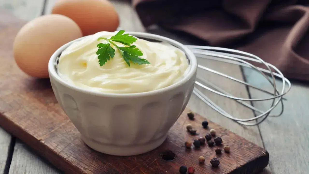 Frische Eier und Petersilie auf einem Holzbrett, bereit, um köstliche Mayonnaise selber machen. Ein Schneebesen liegt daneben.