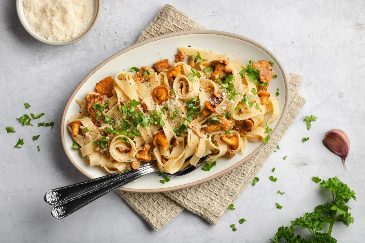 Tagliatelle mit Pfifferlingen, garniert mit Petersilie und Parmesan. Ein köstliches Herbstgericht, das die Aromen der Natur einfängt.