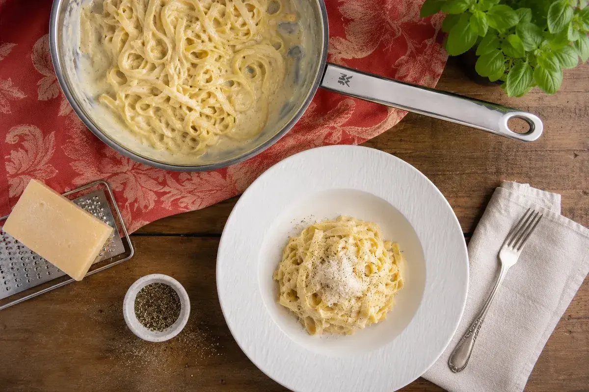 Cremige Pasta Alfredo, zubereitet nach einem einfachen Rezept. Serviert auf einem Teller mit frisch geriebenem Parmesan und Pfeffer.