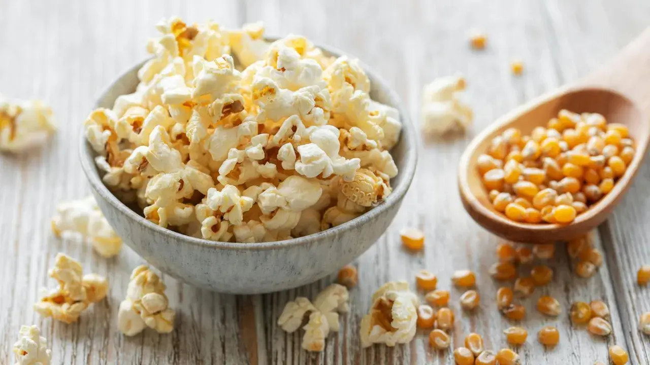 Frisch zubereiteter popcorn im topf, dane Maiskörner auf einem Holzlöffel.
