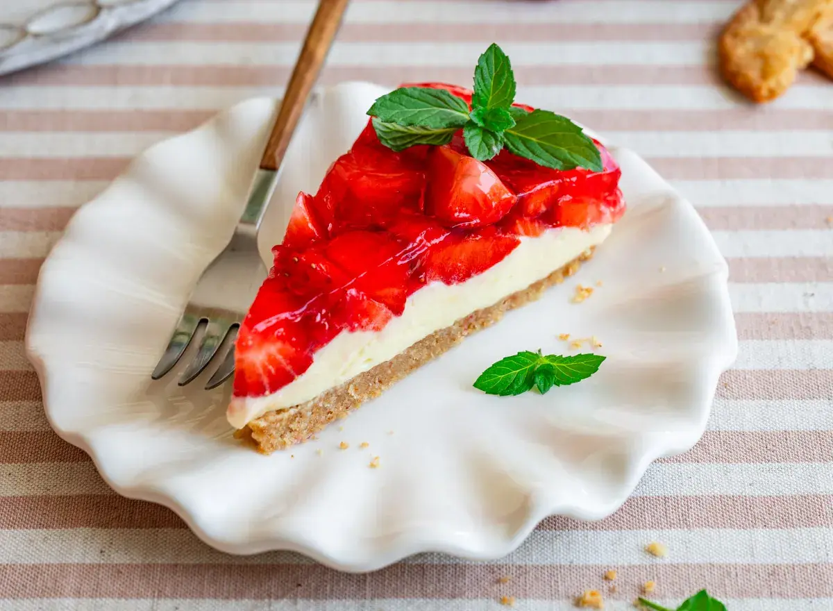 Ein Stück Erdbeerkuchen mit Frischkäsefüllung und glasierten Erdbeeren, garniert mit Minze. Perfekt für einfache Desserts ohne Backen.