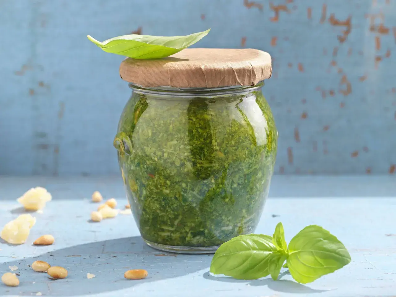 Frisches Pesto im Glas, garniert mit Basilikum. Zutaten wie Pinienkerne und Parmesan liegen daneben. Ein tolles pesto rezept!
