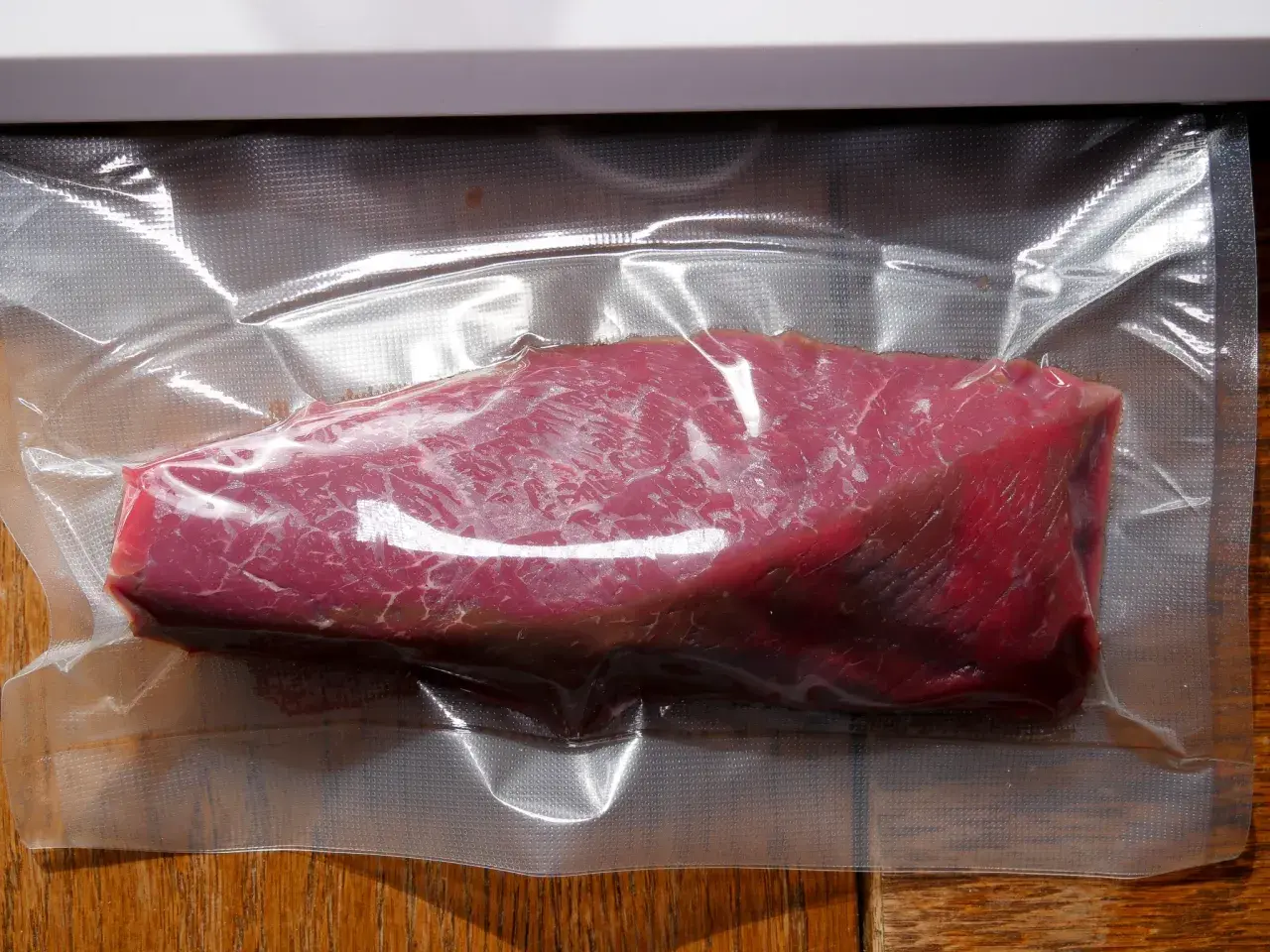 Ein roher Kalbstafelspitz, vakuumiert für Sous-Vide-Garen, liegt auf einem Holztisch.