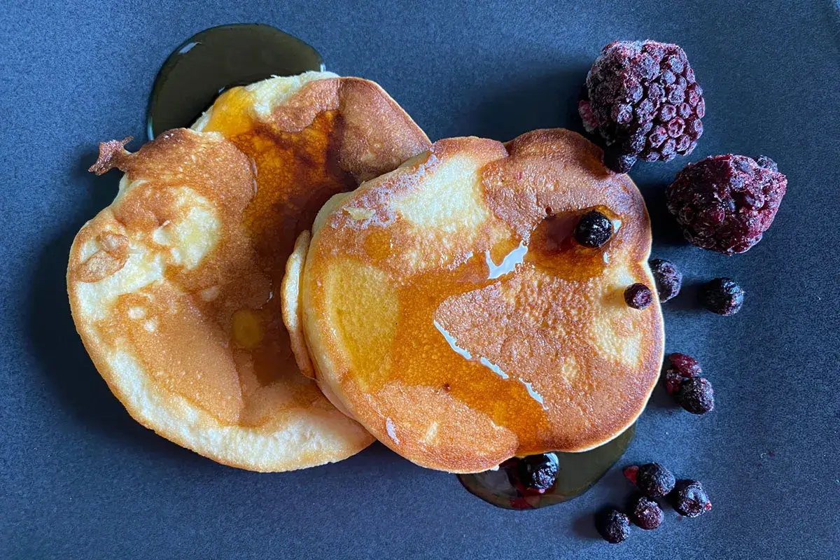 Goldbraune Pfannkuchen ohne Backpulver, beträufelt mit Sirup und garniert mit gefrorenen Beeren. Ein Genuss!