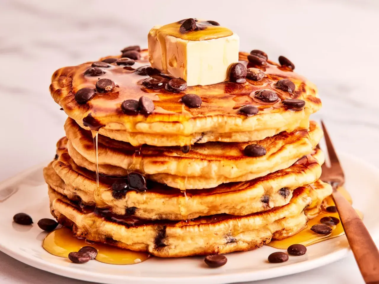 Ein Stapel saftiger Schokoladensplitter-Pfannkuchen, übergossen mit Ahornsirup und einem Stück Butter.