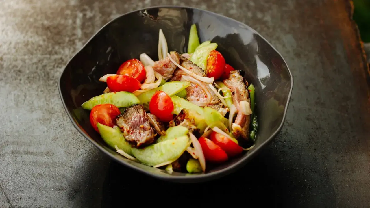 Ein herzhafter Yam Nua Salat mit gegrilltem Rindfleisch, Tomaten und Gurken in einer dunklen Schüssel.