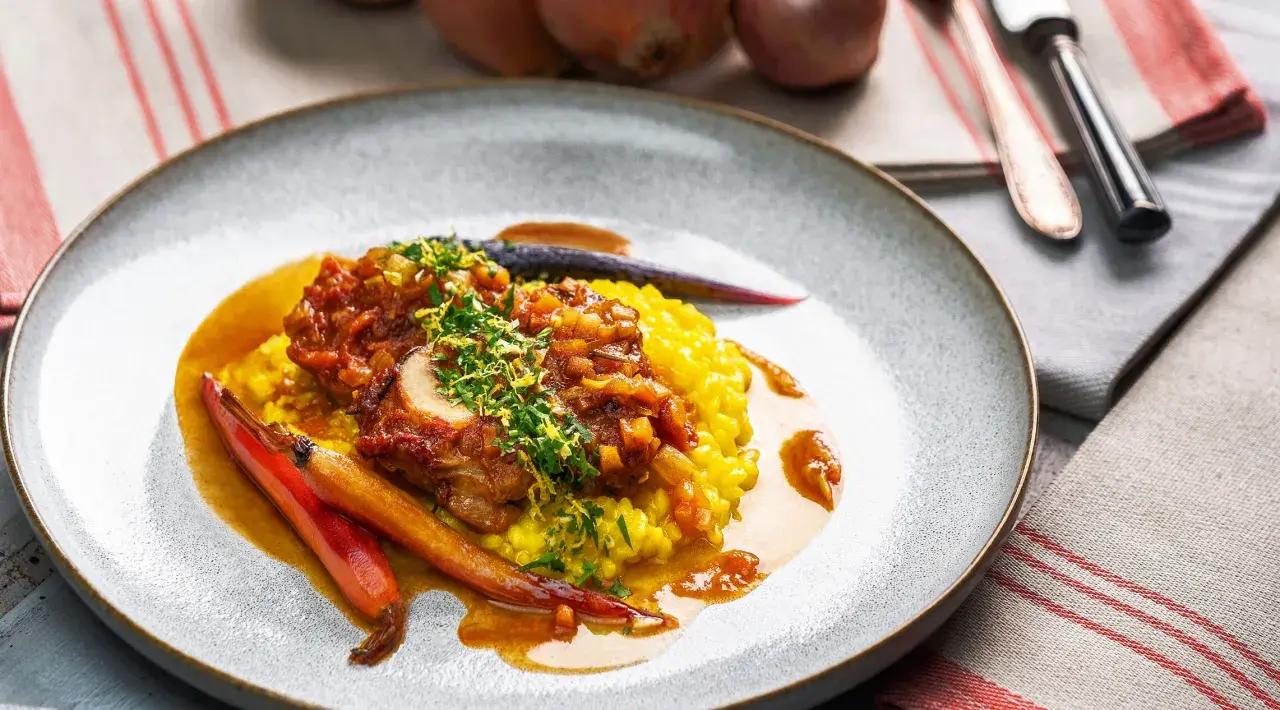 Ein köstliches Ossobuco Rezept mit zartem Kalbfleisch, serviert auf cremigem Safranrisotto und garniert mit frischen Kräutern und karamellisierten Karotten.