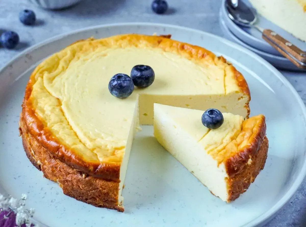 Leckerer protein cheesecake aus magerquark, garniert mit Blaubeeren. Ein Stück ist bereits angeschnitten.