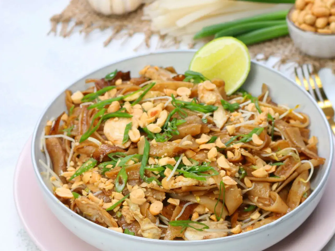 Schüssel mit Pad Thai Gai, garniert mit Erdnüssen und Frühlingszwiebeln, dazu eine Limettenspalte.