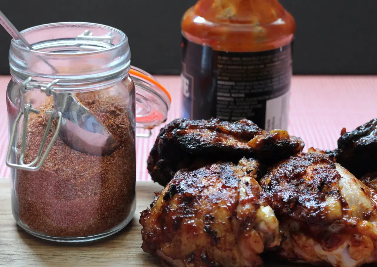 Glas mit Gewürzmischung, perfekt für ein magic dust rezept. Daneben saftige, gegrillte Hähnchenteile und eine Flasche BBQ-Sauce.
