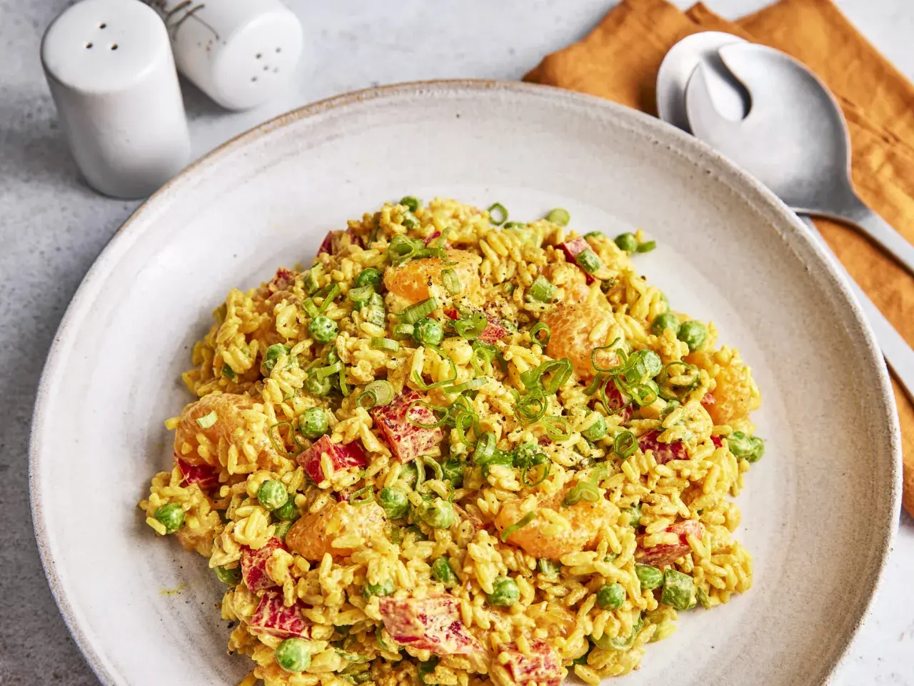 Ein Teller mit weltbestem Reissalat mit Curry, garniert mit Erbsen, Paprika und Frühlingszwiebeln.