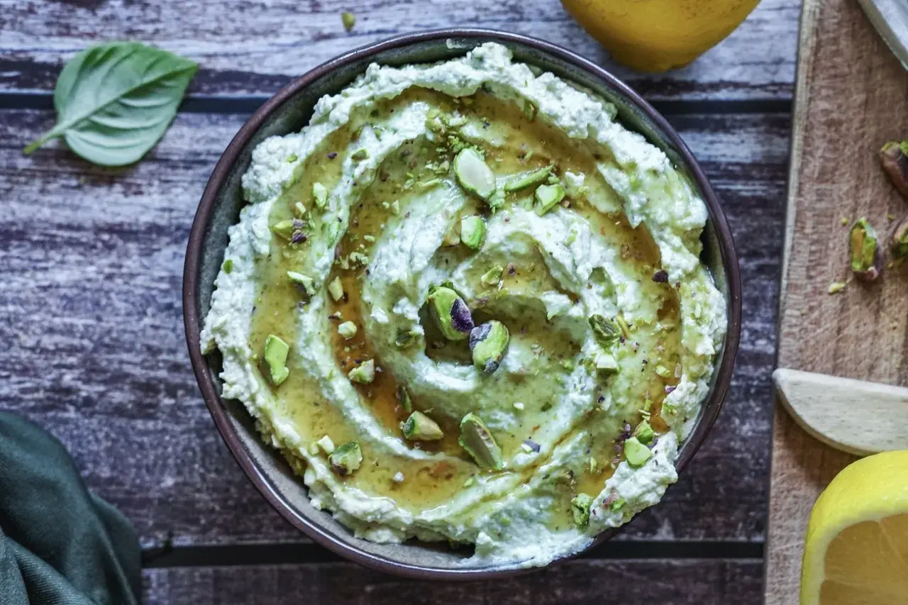 Cremiges Avocado Basilikum Pesto mit Pistazien und Honig beträufelt, garniert mit frischen Basilikumblättern und Zitronenspalten.