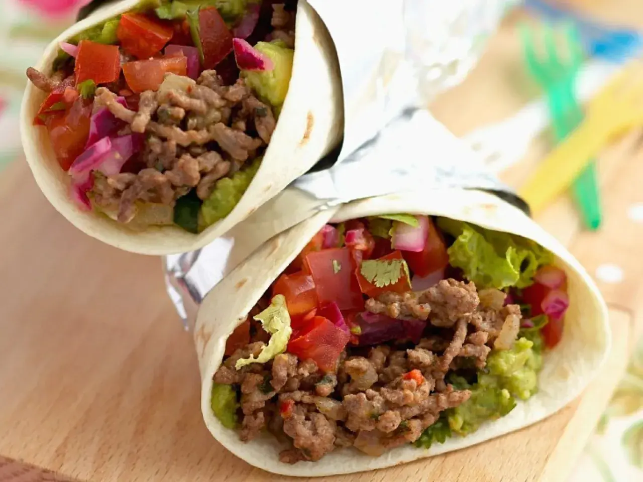 Zwei saftige wraps mit hackfleisch, Guacamole, Tomaten und roten Zwiebeln, eingewickelt in Folie.
