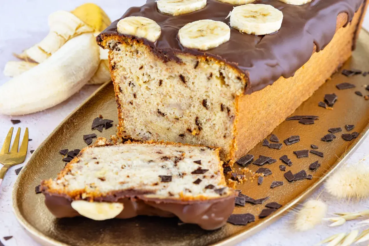 Saftiger Bananen Buttermilch Kuchen mit Schokoladenglasur und Bananenscheiben, garniert mit Schokostückchen.